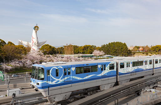 Osaka, Japan - April 1 2021: Special vehicle of Osaka Monorail showing appreciation for healthcare workers, passing Expo '70 Commemorative Park with cherry blossoms in full bloom