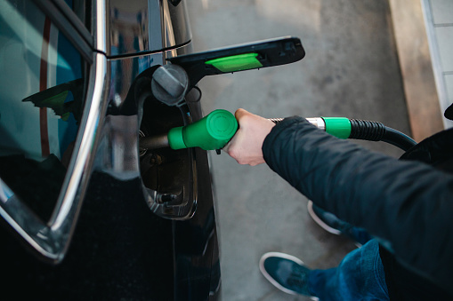 Above view of a male hand holding a gas pump, pumping gasoline into his car