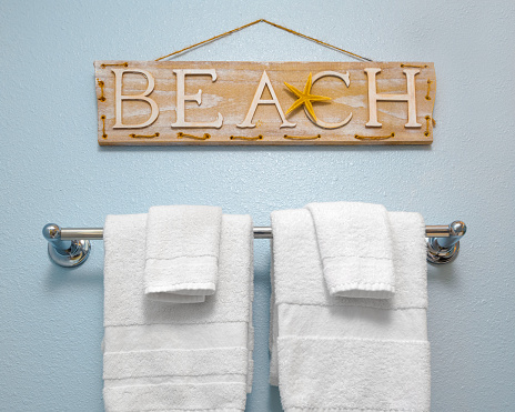 Beach sign above bathroom towel rack with towels and facecloth