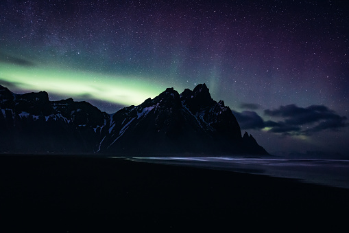 Vestrahorn Mountain Range Polar Lights - Northern Lights Aurora Panorama, Stokkness, Southeast Iceland. Volcanic Black Beach at Vestrahorn Mountain with unedited natural polar lights - northern lights aurora in wintertime. Moody Sky ,Black Beach, Sea and famous Mountain Range. Aurora Night Skyscape. Vestrahorn Mountain Range, Stokkness, South East Iceland, Nordic Countries, Northern Europe.