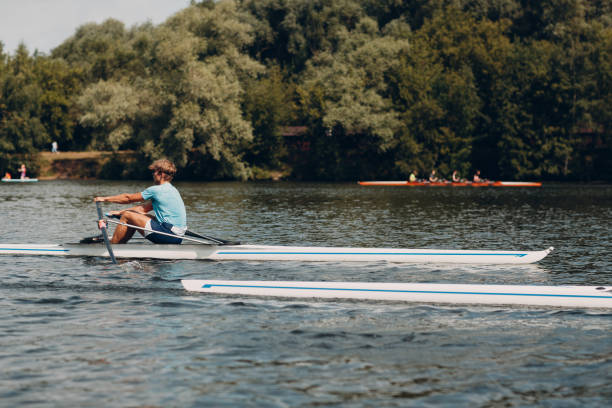 People kayaking and boating on a calm river next to a sandy shore and a green forest
