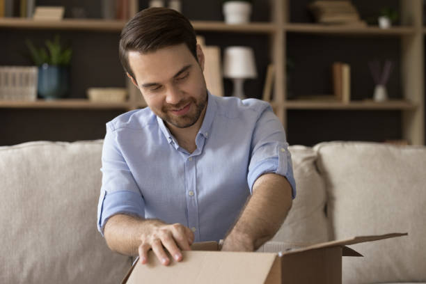 istock Curious smiling young man unpacking carton box. 1387372811