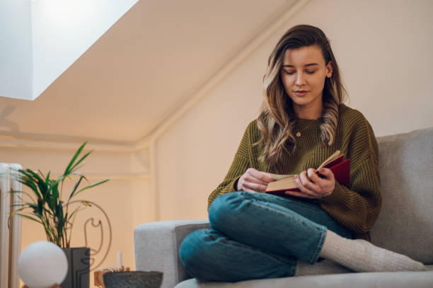 istock Woman reading a book while sitting on the couch at home 1387373421