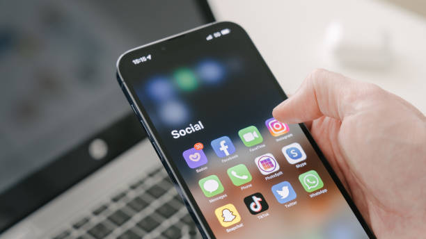 A man's hand holds a Iphone 13 Pro max Gothenburg, Sweden - March 23, 2022: A man's hand holds a Iphone 13 Pro max with social media apps, against the background of a laptop. Blurred background. Selective focus. mobile app stock pictures, royalty-free photos & images