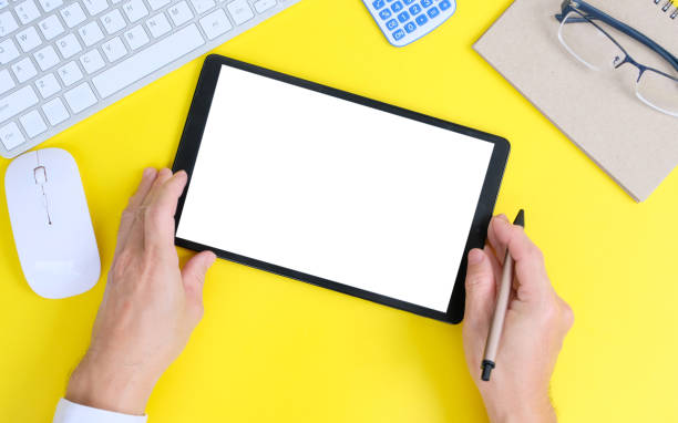 istock Hands holding a tablet computer with an isolated screen and a business desk with a PC, wireless mouse, and keyboard business-related items 1387376294