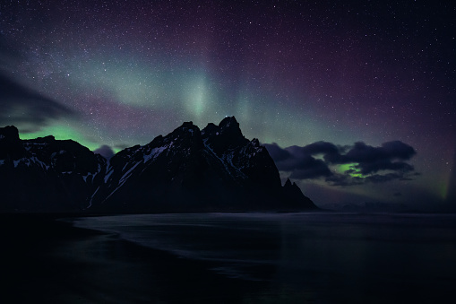 Majestic Vestrahorn Mountain Range Polar Lights - Northern Lights Aurora at Stokksnes, Southeast Iceland. Volcanic Black Beach at Vestrahorn Mountain with natural polar lights - northern lights aurora in wintertime. Moody Sky ,Black Beach, Sea and famous Mountain Range. Aurora Night Skyscape. Vestrahorn Mountain Range, Stokksnes, South East Iceland, Nordic Countries, Northern Europe.