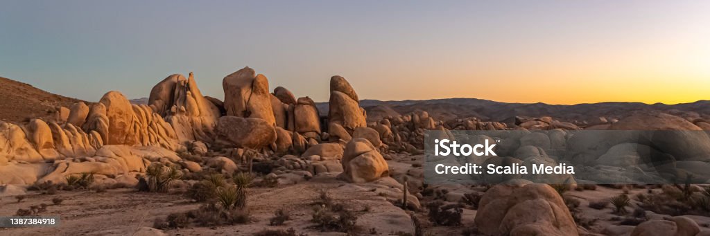 Sunset in Joshua Tree National Park Panoramic sunset with orange, purple, pink gradient sky and rock, boulders covering the Mojave Desert landscape. Palm Springs - California Stock Photo