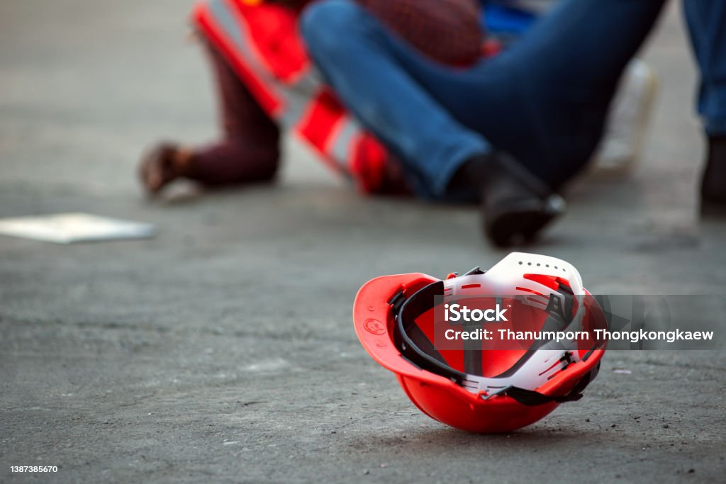 Red hard safety helmet hat for engineer on concrete ground with African-American male engineers injured the accident from working  blurred image background. Construction Site Stock Photo