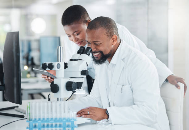 scatto di due scienziati che usano microscopi in un laboratorio - research smiling scientist women foto e immagini stock