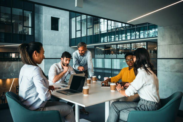 empresários em roupas casuais inteligentes estão discutindo documentos e usando um laptop enquanto co-trabalham no escritório - computer team young adult smart casual - fotografias e filmes do acervo