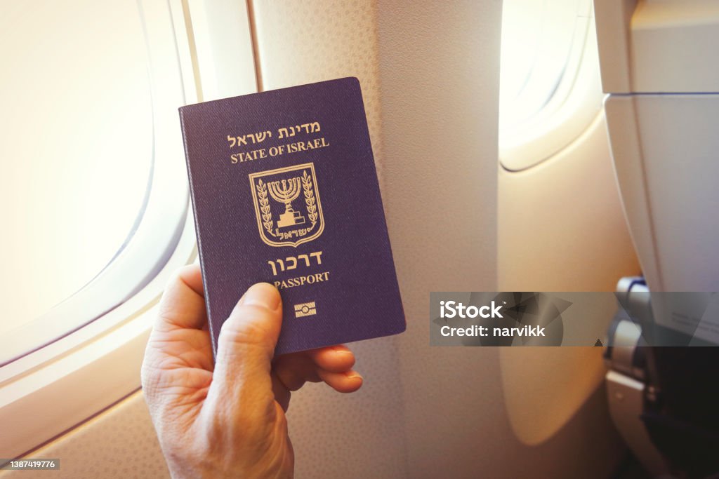 Passenger holding Israeli passport on the airplane Detail of passenger's hand holding passport of the state of Israel on the airplane Israel Stock Photo