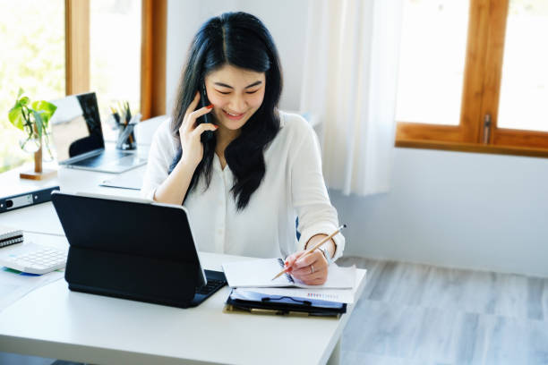 relations d’affaires, un secrétaire d’entreprise asiatique est au téléphone avec les clients vient à contacter en utilisant un stylo pour écrire le temps de résumer le calendrier de travail du propriétaire de l’entreprise. - dealings photos et images de collection