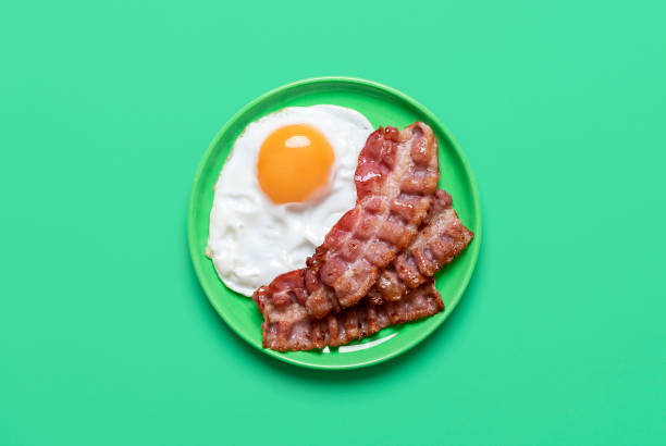 Fried egg and bacon on a green background, above view