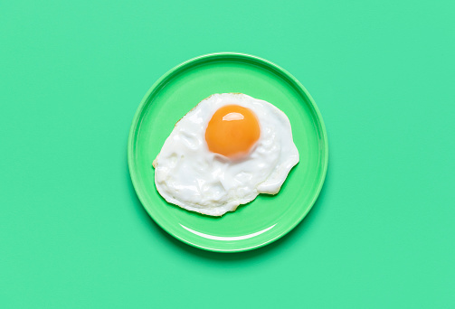 Single fried egg in a plate minimalist on a green table. Top view with a fried egg isolated on a colorful background.