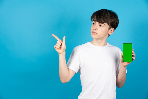 Teenager holding phone with chroma screen and pointing to side copy space