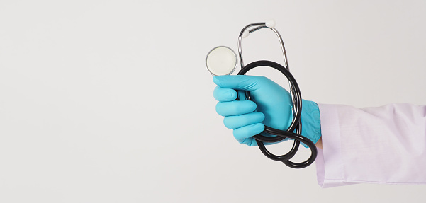 Close up of doctor hand holding stethoscope.Hand wear the blue medical glove and a long-sleeve gown on white background.