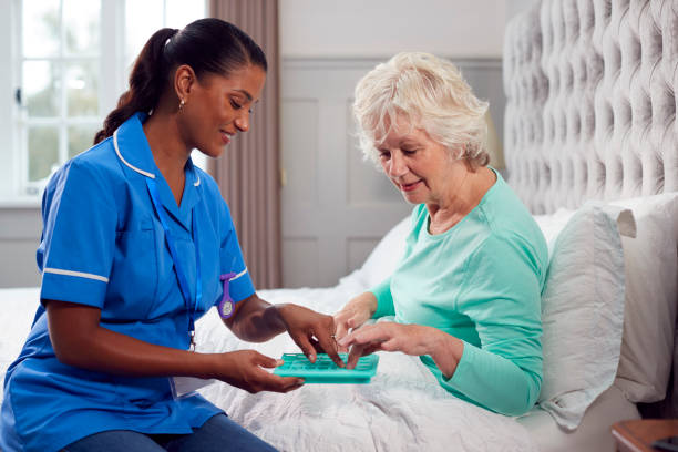 Female Care Worker In Uniform Helping Senior Woman At Home In Bed With Medication stock photo