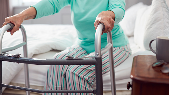 Close Up Of Senior Woman At Home Using Walking Frame To Get Out Of Bed