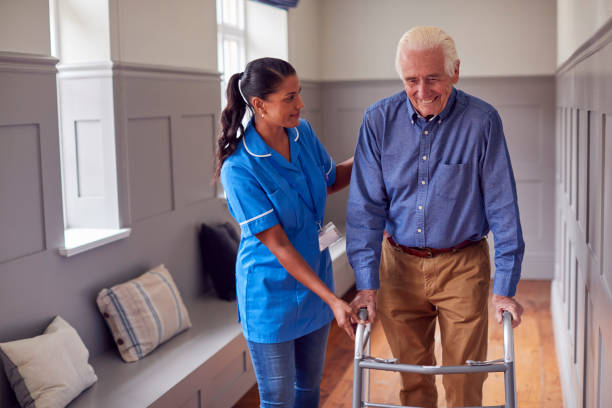 istock Senior Man At Home Using Walking Frame Being Helped By Female Care Worker In Uniform 1387432007