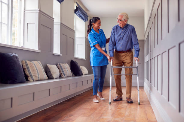 istock Senior Man At Home Using Walking Frame Being Helped By Female Care Worker In Uniform 1387432051
