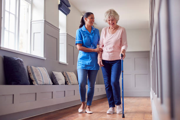 senior woman at home using walking stick being helped by female care worker in uniform - community outreach home caregiver care cheerful imagens e fotografias de stock