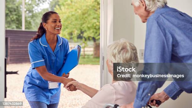 Senior Couple With Woman In Wheelchair Greeting Nurse Or Care Worker Making Home Visit At Door Stock Photo - Download Image Now