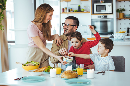 Happy family eating together in the kitchen. Dad and boy take tomatoes. Everyone is happy and satisfied. Home recreation and food preparation on weekends. The concept of community and enjoyment