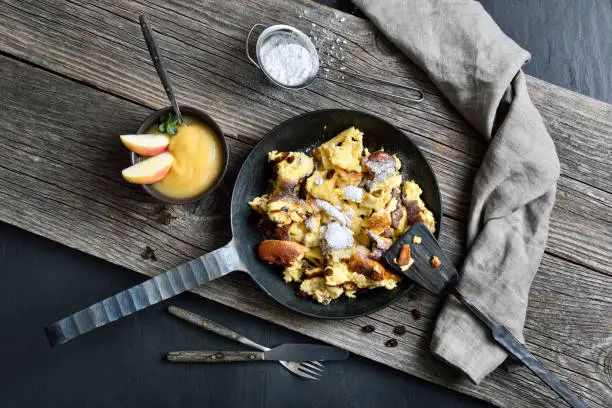 Traditional Viennese Kaiserschmarrn, shredded sweet pancakes with raisins, served in an iron frying pan on old wooden planks on a slate plate