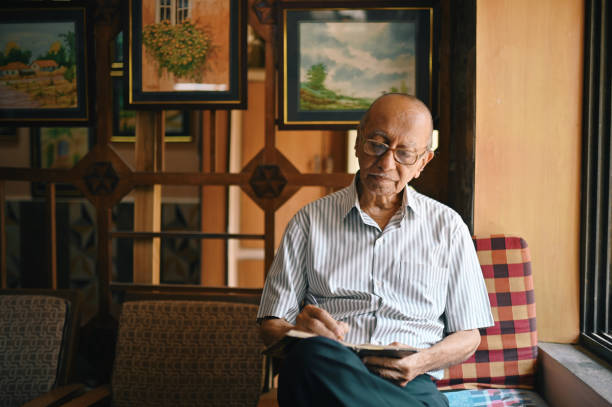 istock Senior man sitting next to window and writing in a diary 1387434667