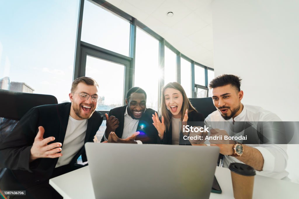Group of business partners sit in front of a laptop and rejoice in the success of their company Teamwork Stock Photo