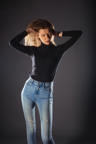 A fashionable young woman in black roll neck posing isolated on a dark background