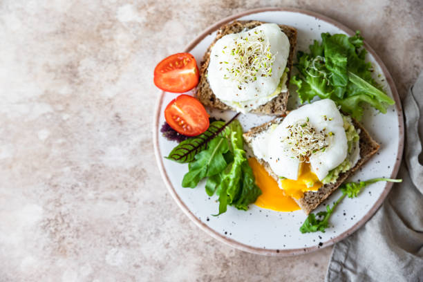 istock Sourdough bread with cream cheese, mashed avocado and poached egg served with salad leaves, tomatoes and sprouts. Healthy breakfast or brunch. Diet food concept. 1387440713