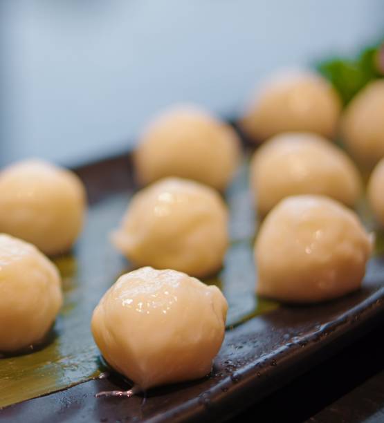 Fresh raw small white fish balls for hot pot on black plate close up view