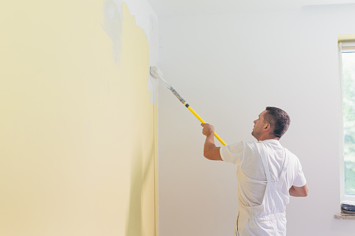 Worker man applies paint and putty to the walls in the apartment, makes repairs in a new house