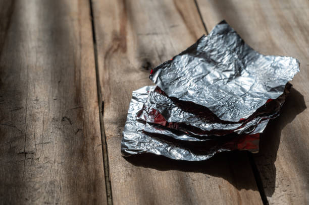 istock A stack of rectangular aluminum candy wrappers against a wooden background. Rough, cracked boards. Natural lighting. 1387442204