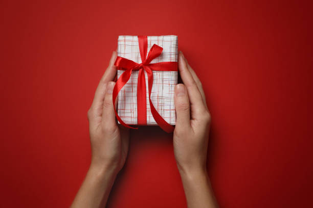 istock Woman holding Christmas gift on red background, top view 1387444111