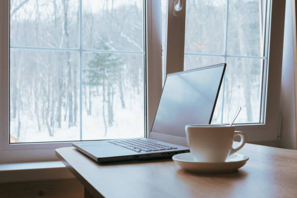 istock Cup and laptop on the table in front of the window. 1387446636