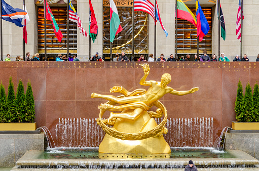 Golden Prometheus statue at Rockefeller Center during winter with flags in the background and people ice skating in the forefront, New York City, horizontal