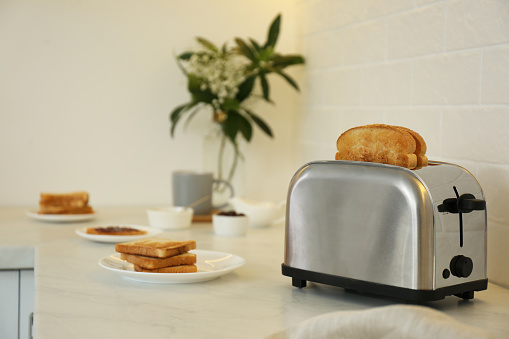 A shiny metallic toaster in action with some red yellow glow. With reflection and isolated on white background.