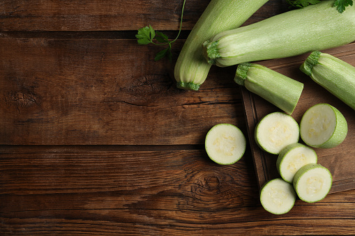 Cut and whole ripe zucchinis on wooden table, flat lay. Space for text