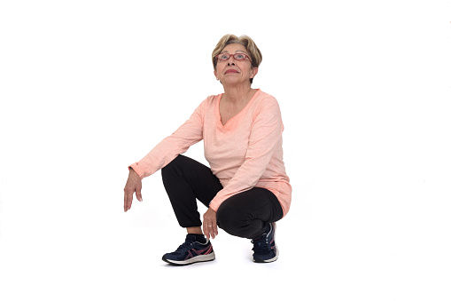 front view of a  senior woman squatting and looking up on white backgrond