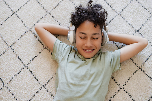 High angle view of a teenage boy laying on the carpet and feeling comfortable. He is listening to music.