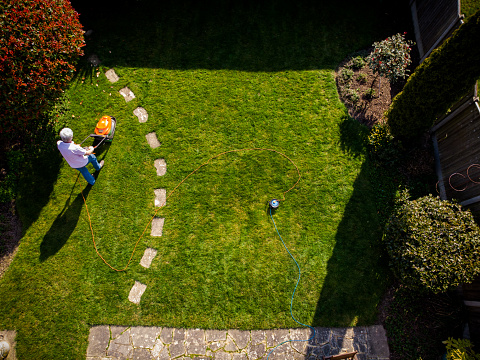 Aerial topdown view, taken by drone, depicting one man mowing his lawn with a lawnmower in his garden.