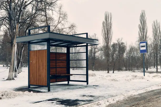 Photo of Empty bus stop, it is sleet, there is a lot of snow on the road and the walking path, the sky is full of clouds