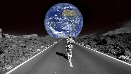 Person in a space suit walking on the road on the moon. Distant planet earth visible in the background
