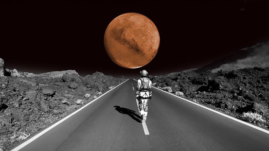 Person in a space suit walking on the road on the moon. Distant planet mars visible in the background