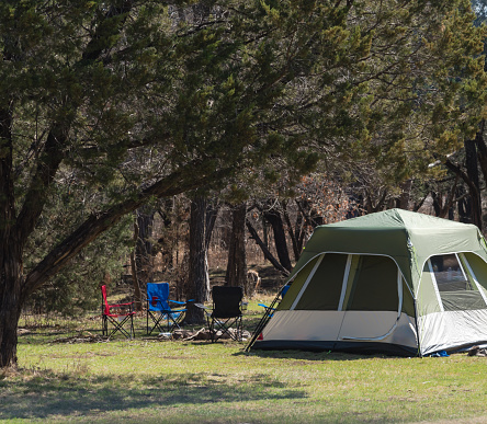 Family camping tent with folding chairs under tree shade at camping site in national park of Oklahoma, America. Wintertime outdoor and recreational activity