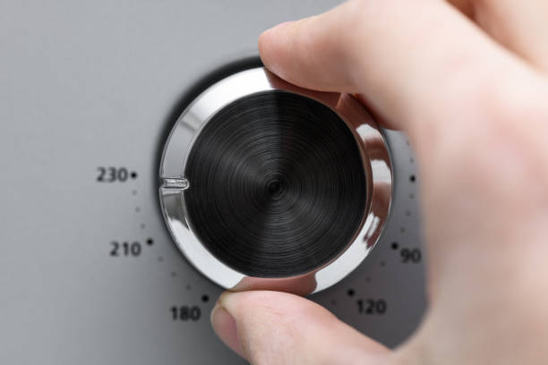 istock Hand twists round temperature adjustment button in the microwave oven. Button to warm food on gray background 1387454513