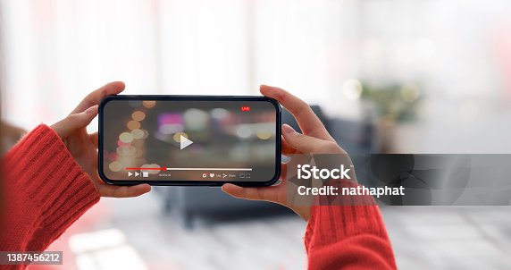 istock Woman holding and watching video via mobile phone in horizontal view at home. 1387456212