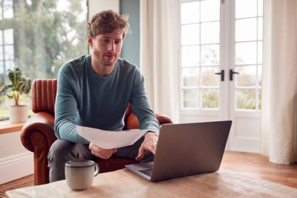 Man Sitting On Armchair At Home With Laptop Paying Bill Online Man Sitting On Armchair At Home With Laptop Paying Bill Online hot desking stock pictures, royalty-free photos & images